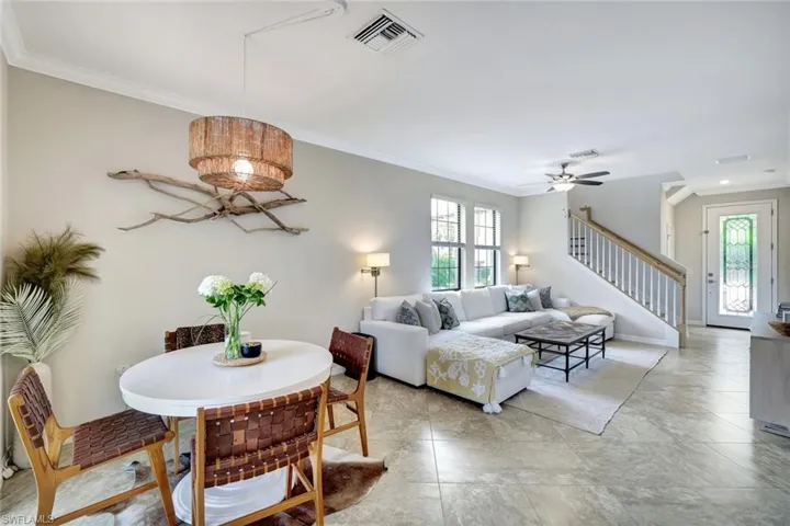 Light and bright dining area open to the living room featuring ceiling fan, crown molding, and tile floors.