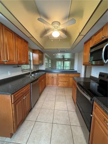 Kitchen featuring stove, dishwasher, a tray ceiling, ceiling fan, and brown cabinetry