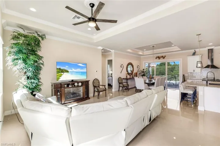 Living room with a tray ceiling, crown molding, recessed lighting, ceiling fan, and light tile patterned floors