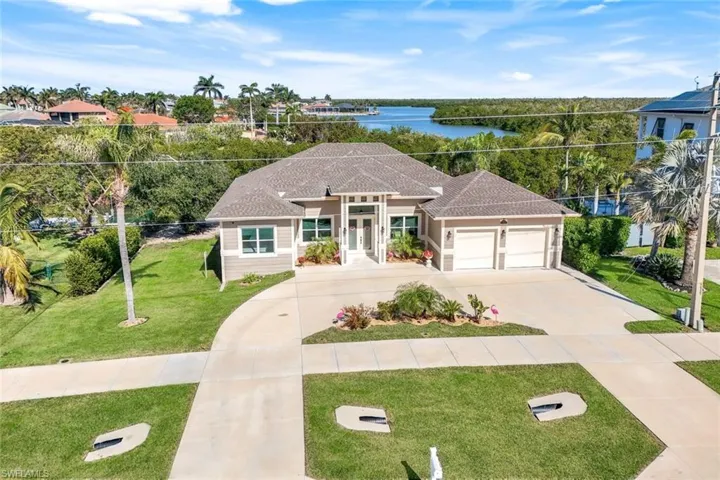 View of front facade with a front lawn, a water view, concrete driveway, a garage, and roof with shingles