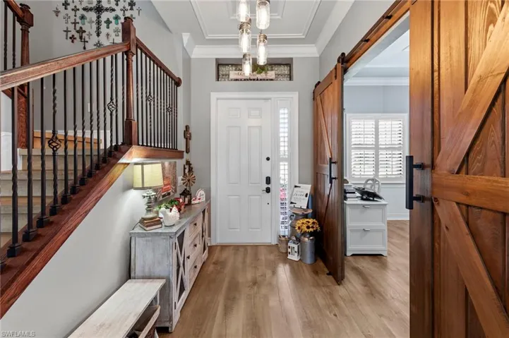 Entrance foyer with a barn door, light wood finished floors, ornamental molding, and stairs