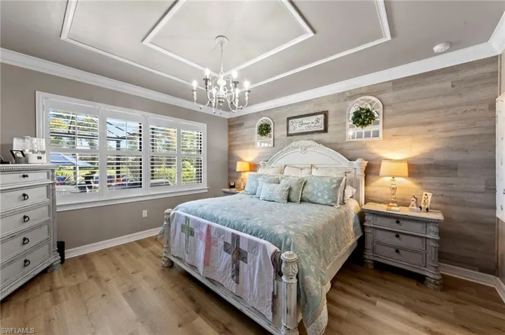 Bedroom featuring light wood finished floors, wood walls, a chandelier, and ornamental molding