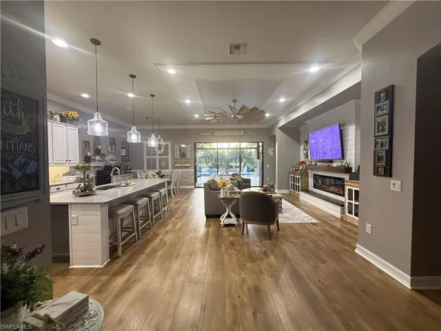Living area featuring ornamental molding, dark wood finished floors, ceiling fan, a glass covered fireplace, and recessed lighting
