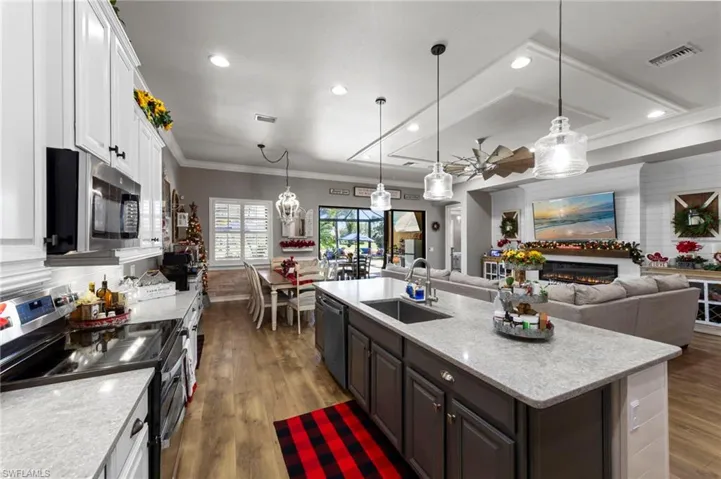 Kitchen featuring appliances with stainless steel finishes, white cabinets, a warm lit fireplace, hanging light fixtures, and dark wood-type flooring