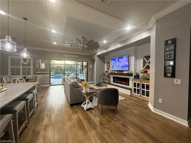 Living area with ornamental molding, dark wood-style flooring, ceiling fan, a glass covered fireplace, and recessed lighting