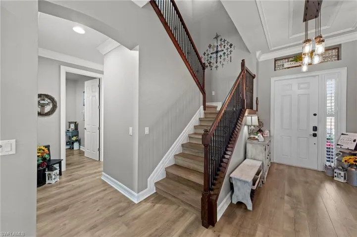 Foyer entrance featuring ornamental molding, light wood-style flooring, stairs, and arched walkways
