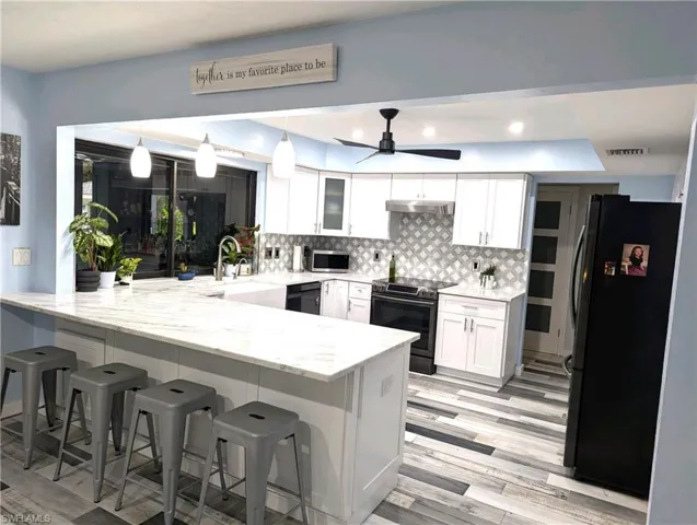 Kitchen featuring a peninsula, decorative backsplash, light stone counters, barn sink and white cabinetry