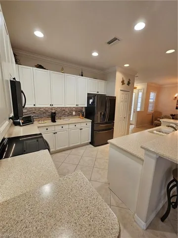 Kitchen with ornamental molding, white cabinets, decorative backsplash, fridge, and stove