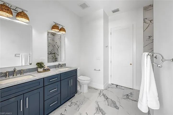 Bathroom with marble look tiles, double vanity, toilet, and baseboards