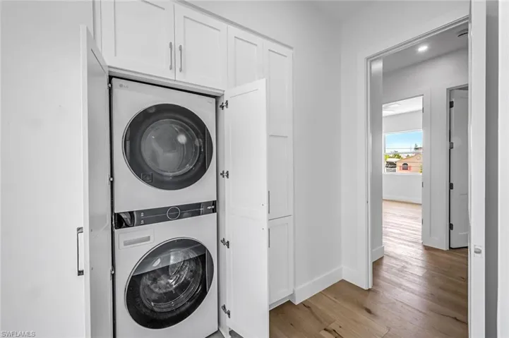 Laundry room featuring stacked washer / drying machine, light wood finished floors, and baseboards