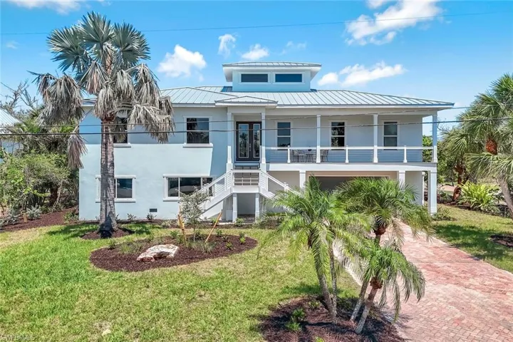 Beach home featuring stairs, a front yard, a porch, stucco siding, and metal roof
