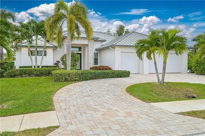 View of front of home with decorative driveway, a front yard, stucco siding, a garage, and a metal roof