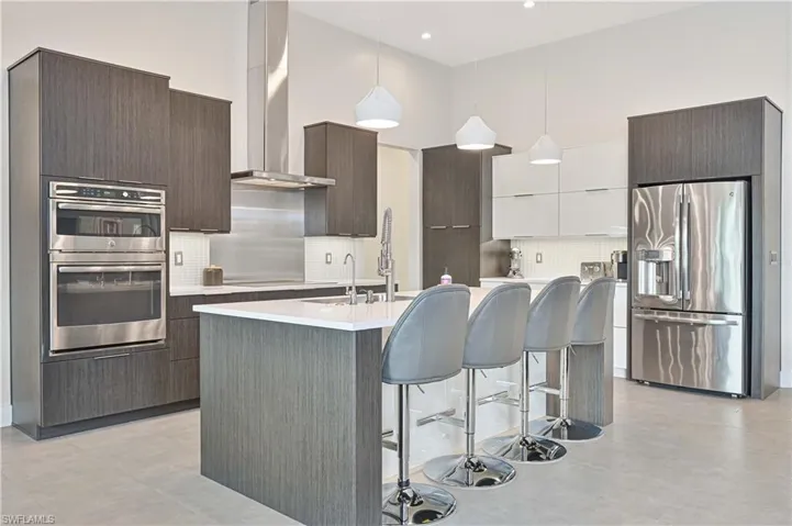 Kitchen featuring modern cabinets, appliances with stainless steel finishes, wall chimney exhaust hood, decorative light fixtures, and a kitchen bar