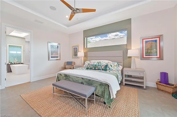 Bedroom with a raised ceiling, ceiling fan, crown molding, and ensuite bath