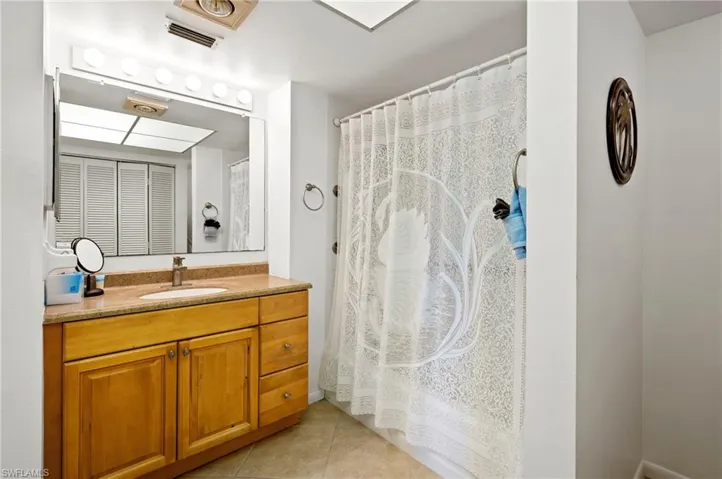 Full bathroom with tile patterned floors, curtained shower, vanity, and visible vents