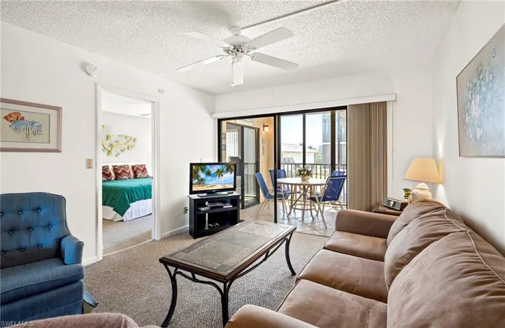 Carpeted living room with a textured ceiling, baseboards, and ceiling fan