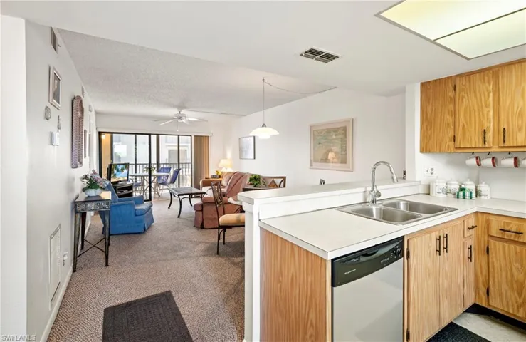 Kitchen with a sink, open floor plan, a peninsula, dishwashing machine, and light colored carpet