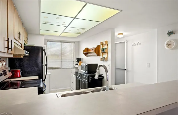 Kitchen with baseboards, a sink, light countertops, appliances with stainless steel finishes, and under cabinet range hood