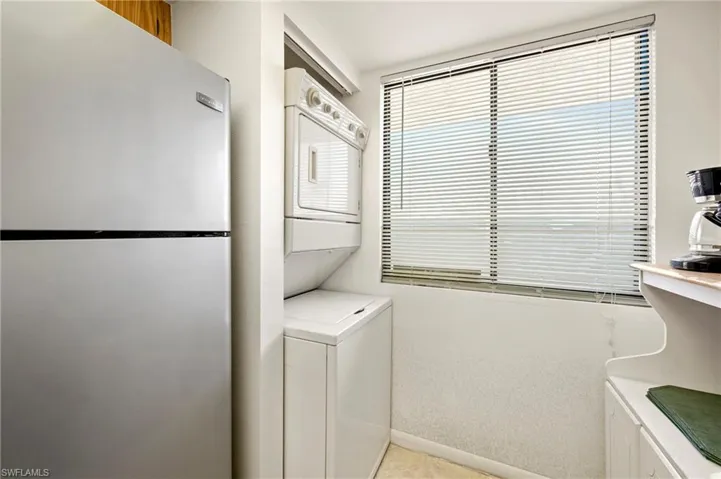 Laundry area with baseboards, stacked washer and clothes dryer, light laminate patterned floors, laundry area, and light colored carpet