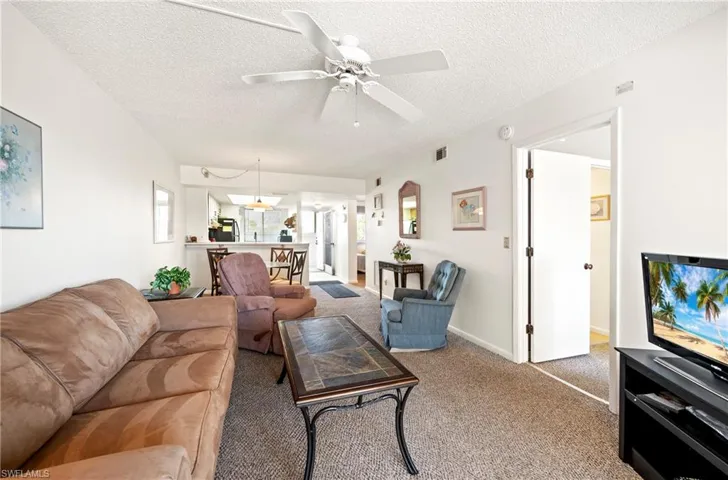 Carpeted living area featuring visible vents, a textured ceiling, and ceiling fan