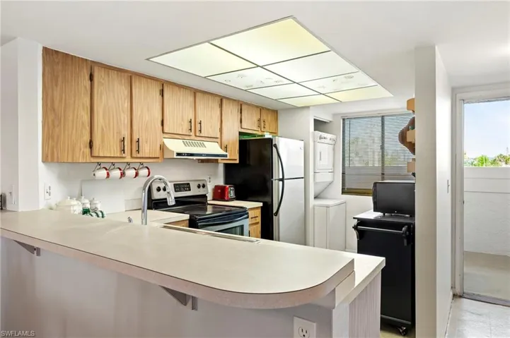 Kitchen featuring light countertops, appliances with stainless steel finishes, a peninsula, under cabinet range hood, and stacked washer and dryer