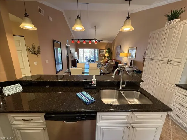 Kitchen with lofted ceiling, pendant lighting, dishwasher, white cabinetry, and dark stone countertops