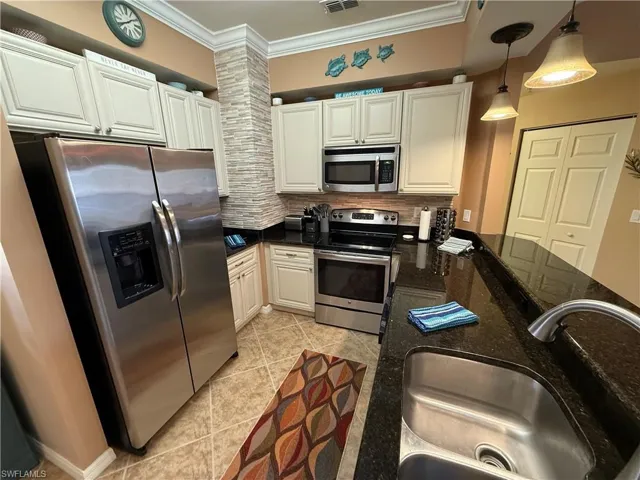 Kitchen featuring stainless steel appliances, dark stone counters, tasteful backsplash, hanging light fixtures, and light tile patterned floors