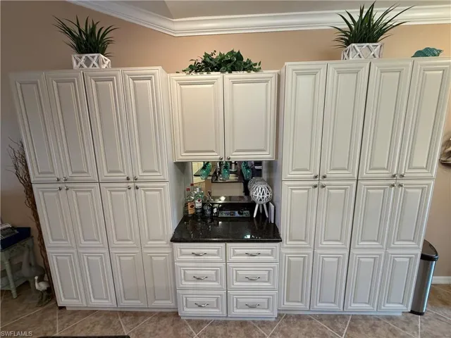 Bar with white cabinets, light tile patterned floors, ornamental molding, and dark stone counters