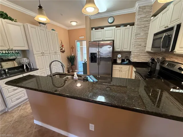 Kitchen featuring appliances with stainless steel finishes, crown molding, dark stone counters, backsplash, and pendant lighting