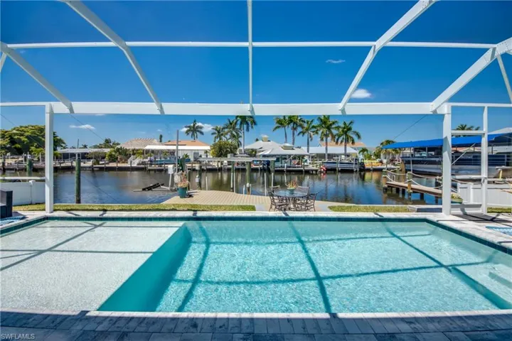 View of pool with glass enclosure, a water view, a patio, and a boat dock