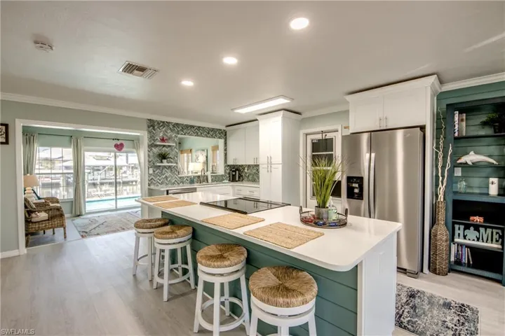 Kitchen featuring white cabinets, a kitchen breakfast bar, stainless steel refrigerator with ice dispenser, black electric cooktop, and tasteful backsplash