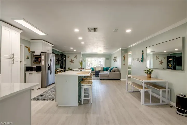 Kitchen featuring white cabinetry, a kitchen breakfast bar, light hardwood / wood-style flooring, appliances with stainless steel finishes, and ornamental molding