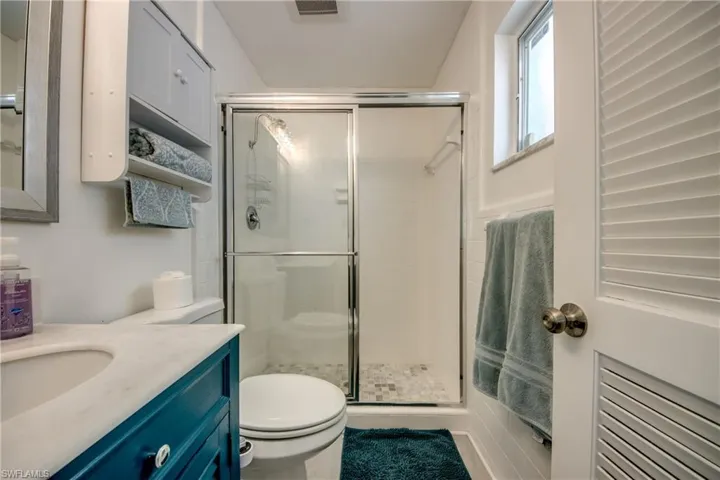 Bathroom featuring vanity, toilet, a shower with door, and radiator heating unit