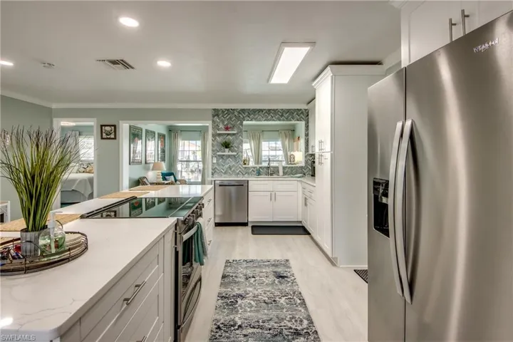 Kitchen featuring light stone countertops, tasteful backsplash, light hardwood / wood-style floors, white cabinets, and appliances with stainless steel finishes