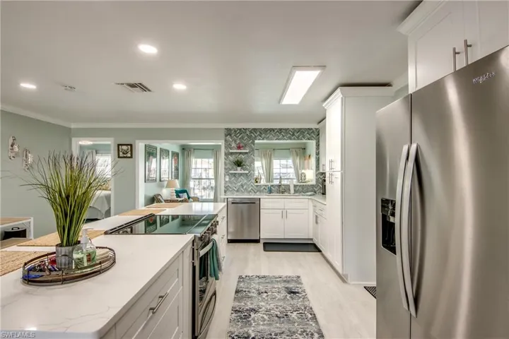Kitchen featuring stainless steel appliances, crown molding, light hardwood / wood-style floors, decorative backsplash, and white cabinets