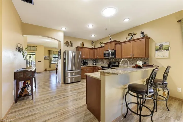 Kitchen with brown cabinets, arched walkways, appliances with stainless steel finishes, a peninsula, and a kitchen breakfast bar