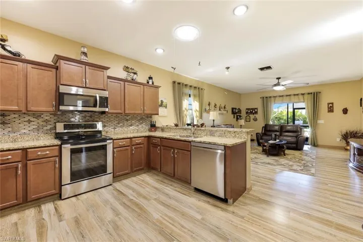 Kitchen featuring brown cabinetry, a peninsula, light stone counters, appliances with stainless steel finishes, and light wood-type flooring