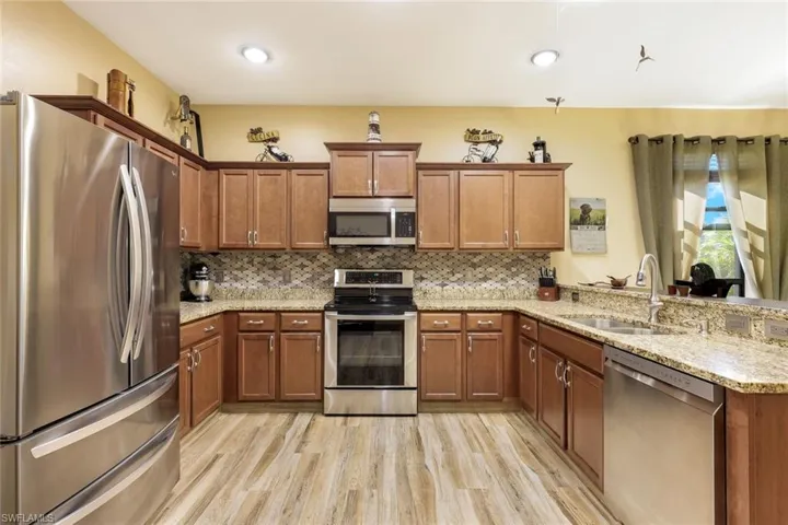 Kitchen featuring stainless steel appliances, brown cabinetry, a peninsula, light stone countertops, and light wood-style flooring