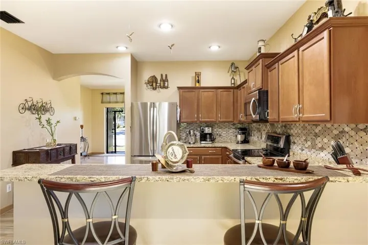 Kitchen with a kitchen breakfast bar, brown cabinetry, appliances with stainless steel finishes, and tasteful backsplash