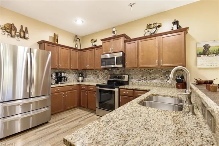 Kitchen featuring stainless steel appliances, brown cabinetry, a peninsula, light stone countertops, and light wood-style flooring