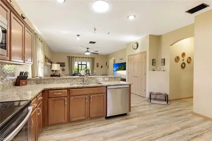 Kitchen featuring brown cabinetry, a peninsula, light stone counters, appliances with stainless steel finishes, and light wood-type flooring
