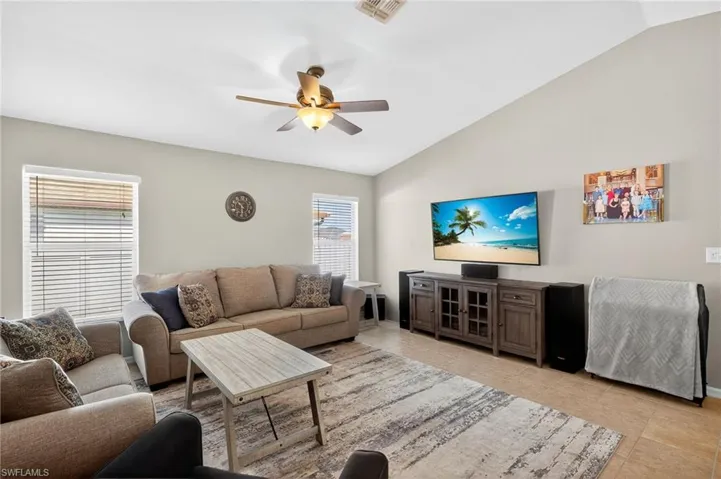Spacious living area open to kitchen with vaulted ceiling, ceiling fan, and light tile patterned floors