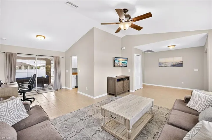 Living room with vaulted ceiling, office area, a ceiling fan, and light tile patterned floors