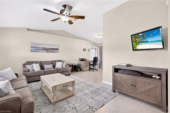 Living room featuring light tile patterned floors, an office area, a ceiling fan, and vaulted ceiling