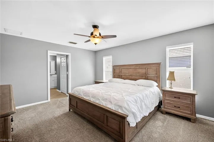 Primary Bedroom with light colored carpet, connected bathroom, and a ceiling fan