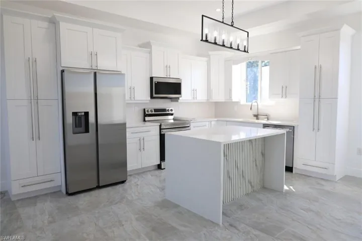 Kitchen with appliances with stainless steel finishes, a kitchen island, pendant lighting, light stone counters, and white cabinets