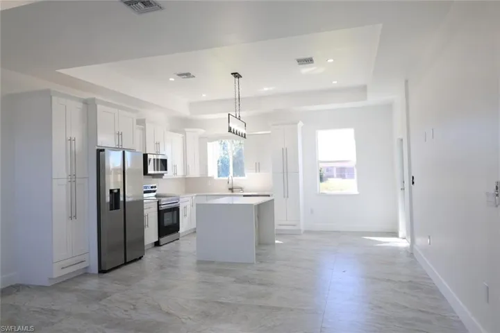 Kitchen with a tray ceiling, stainless steel appliances, white cabinets, and recessed lighting