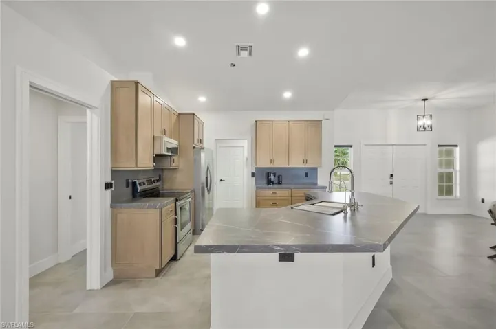 Kitchen featuring stainless steel appliances, light wood finish cabinets, decorative light fixtures, a large island with sink, and a kitchen breakfast bar