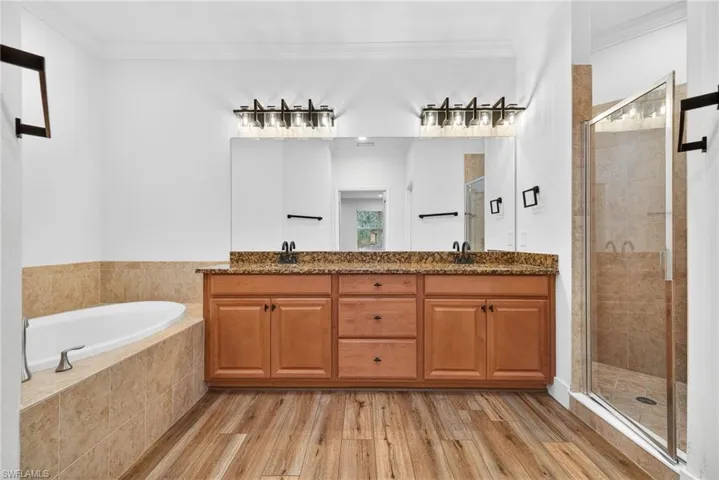 Full bathroom with a stall shower, double vanity, light wood-type flooring, ornamental molding, and a garden tub