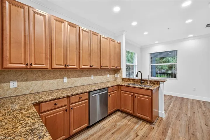 Kitchen featuring dark stone countertops, crown molding, decorative backsplash, light wood-style flooring, and recessed lighting